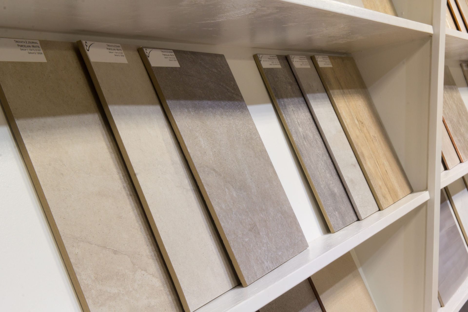 Tile samples on display, various colors and textures, arranged on shelves in a showroom setting.