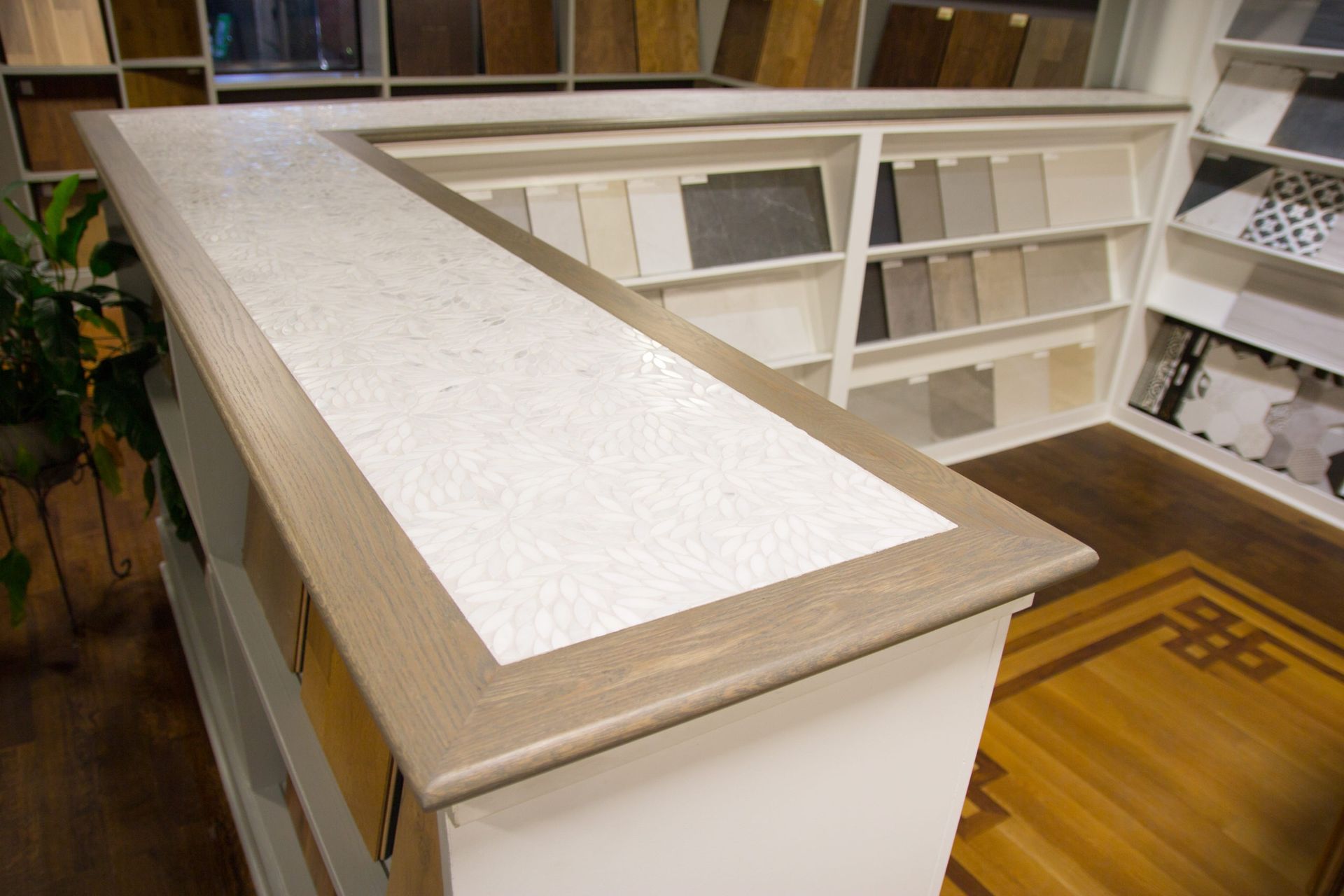 A counter with a white textured surface and wooden trim, displaying flooring samples in a showroom.