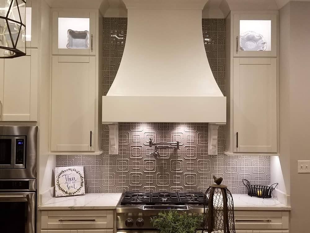 Cream kitchen with range, hood, decorative tile backsplash, and cabinets.