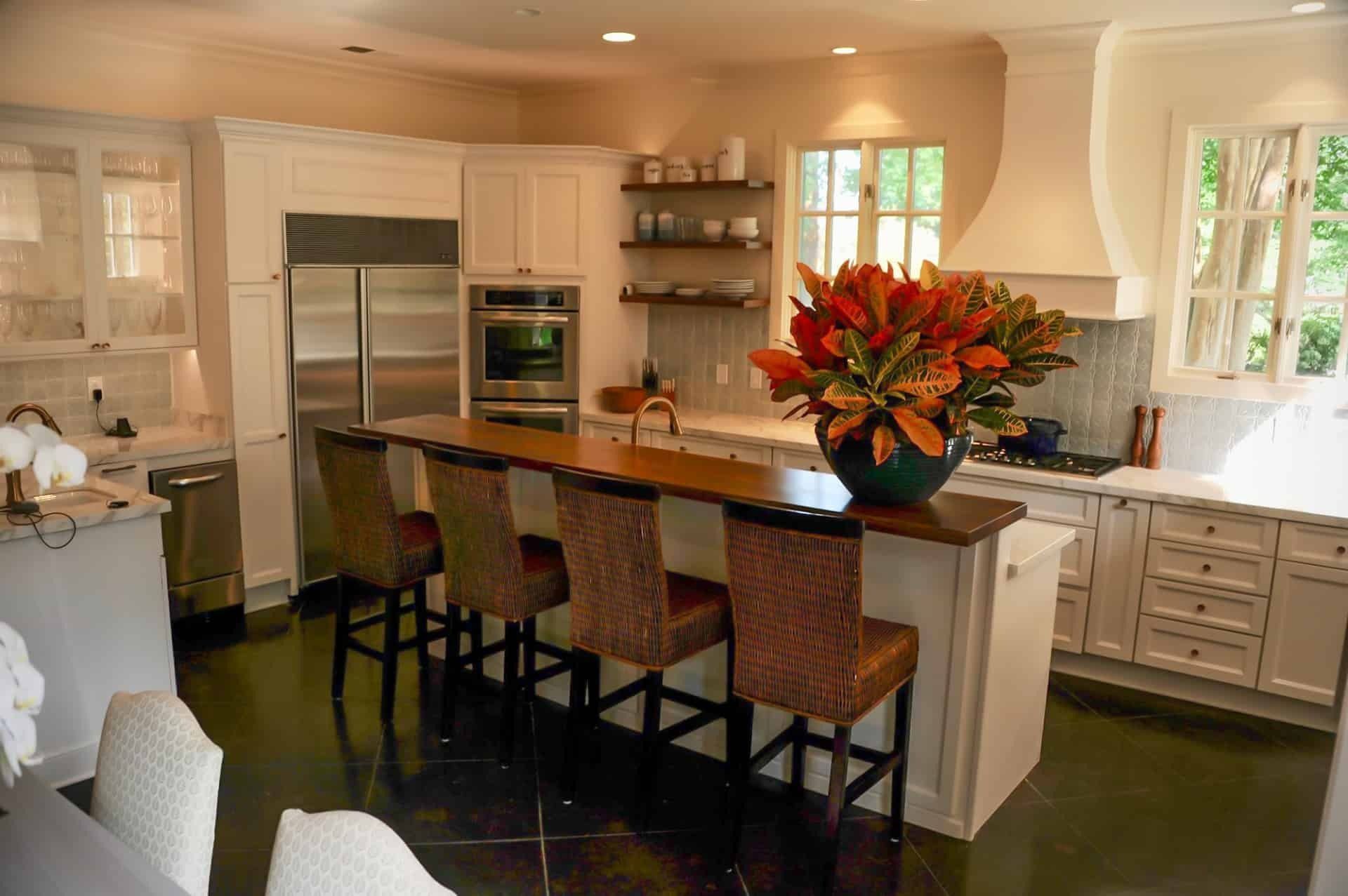 Elegant white kitchen with island seating, stainless steel appliances, and large floral arrangement.