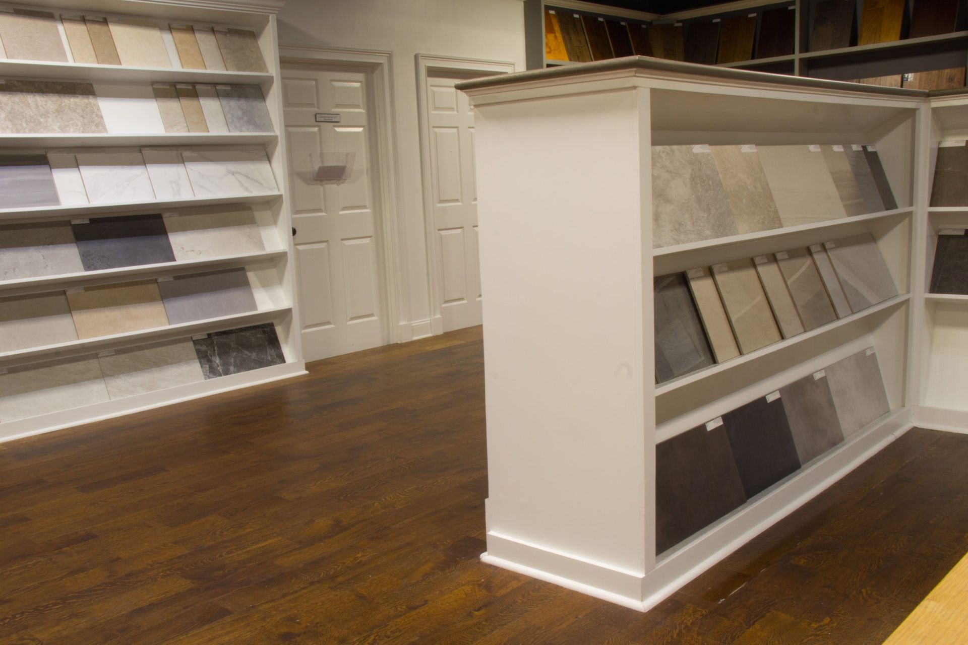 Tile showroom interior with shelves displaying various tile samples, dark wood floors.