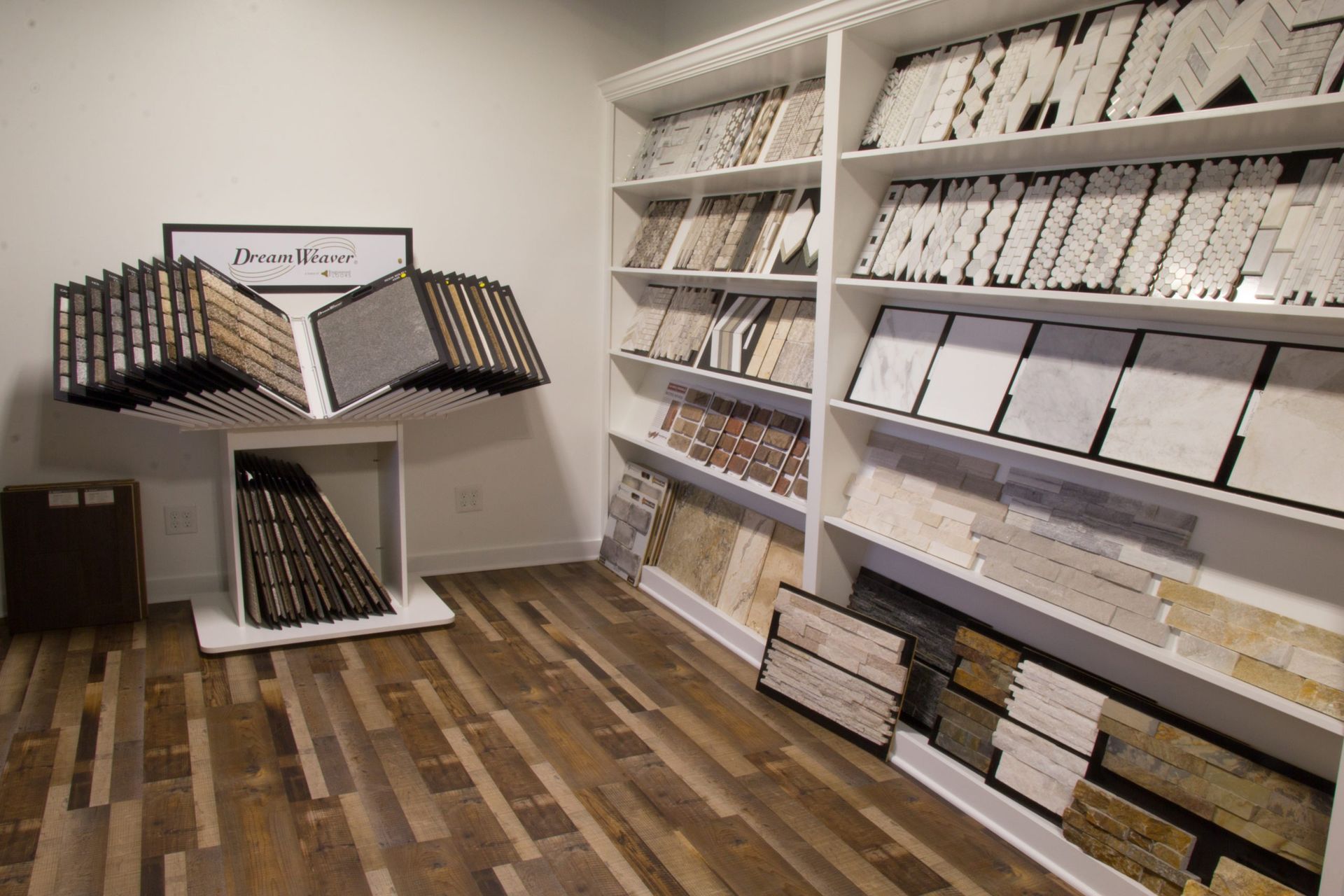 Tile showroom: displays of tile samples on shelves and rotating racks, hardwood floor.