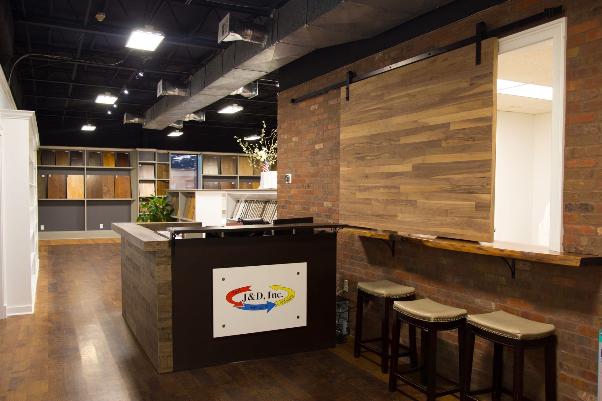 Reception area of a store with wood and brick decor, a desk, and stools.