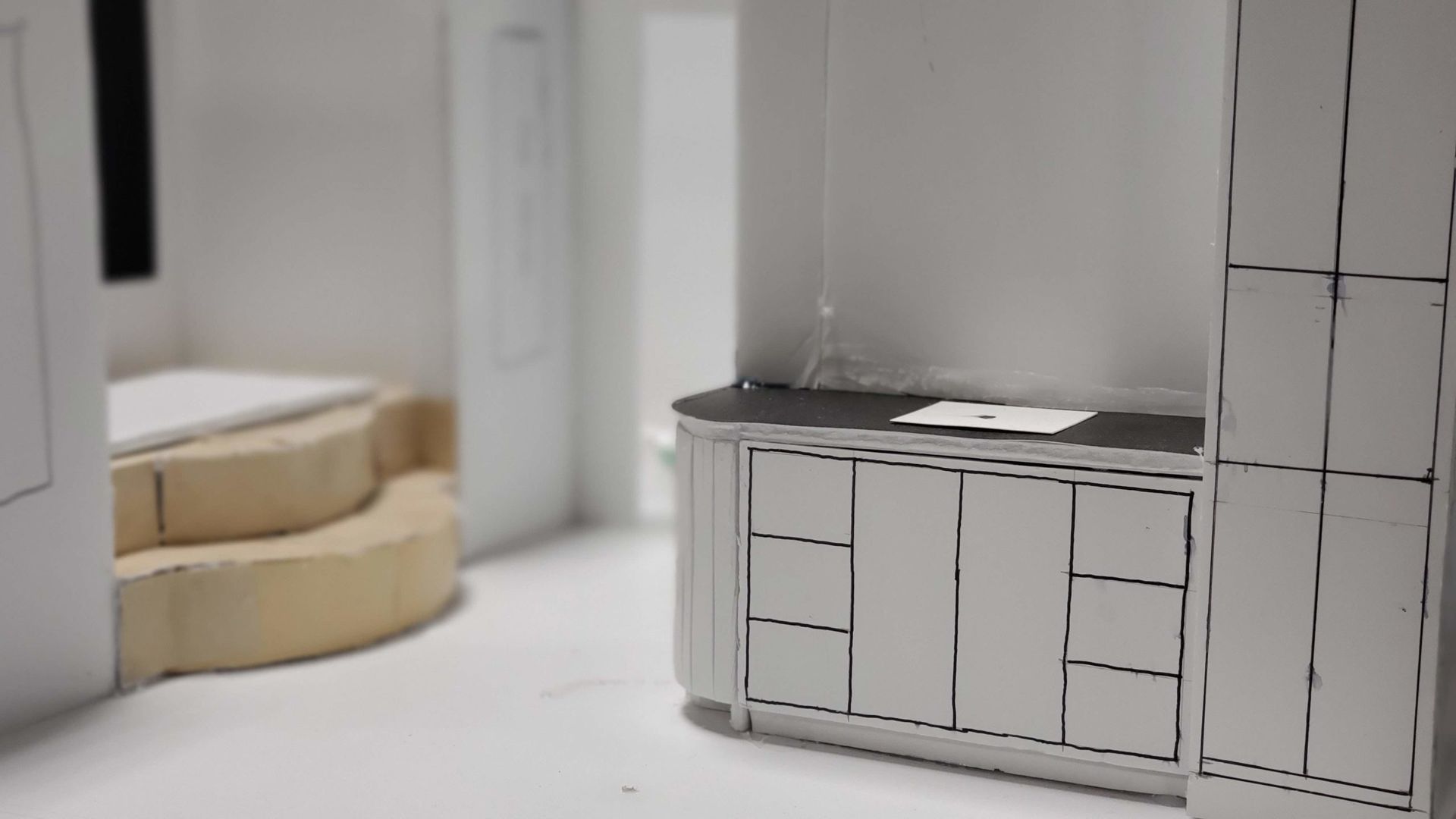 Model kitchen interior with white cabinets and a dark countertop. A staircase is visible.