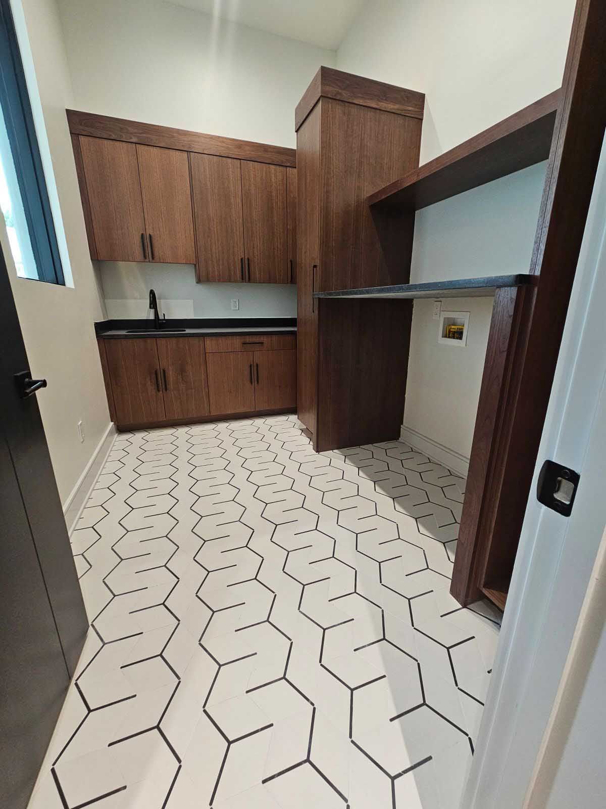 Laundry room with wood cabinets, black countertops, and hexagonal patterned floor tiles.