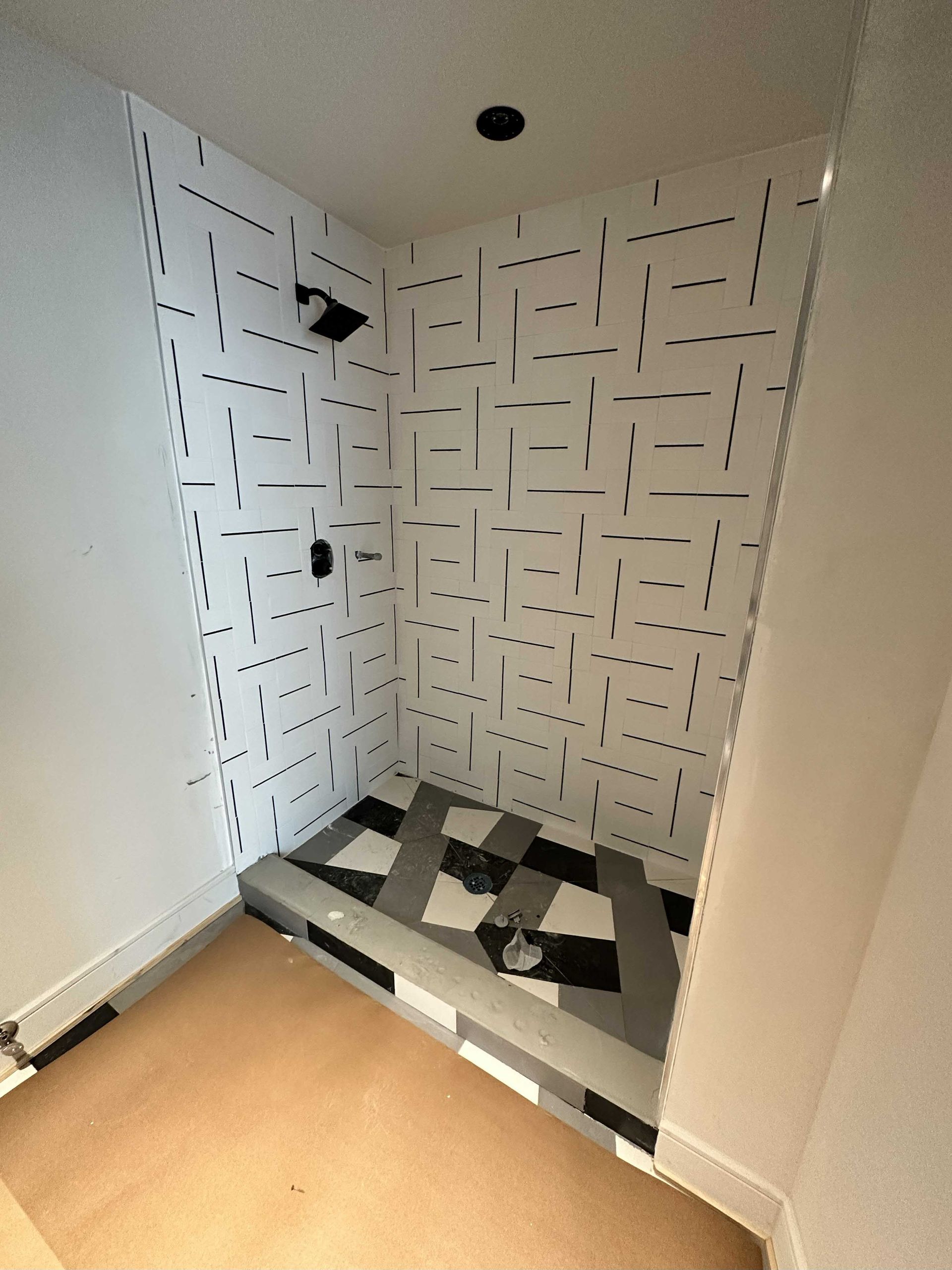 Shower stall with black and white patterned walls and floor, and black fixtures.