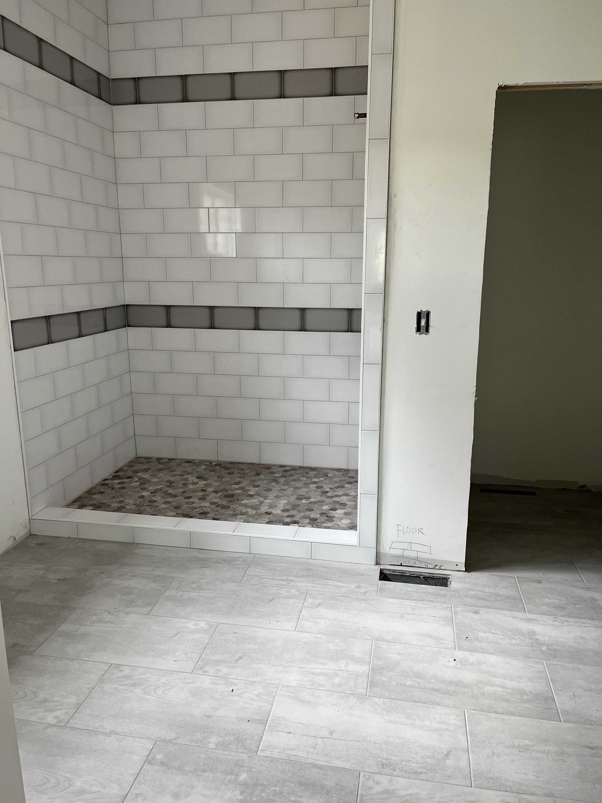 Bathroom under construction; shower with gray stone floor and white tiled walls.