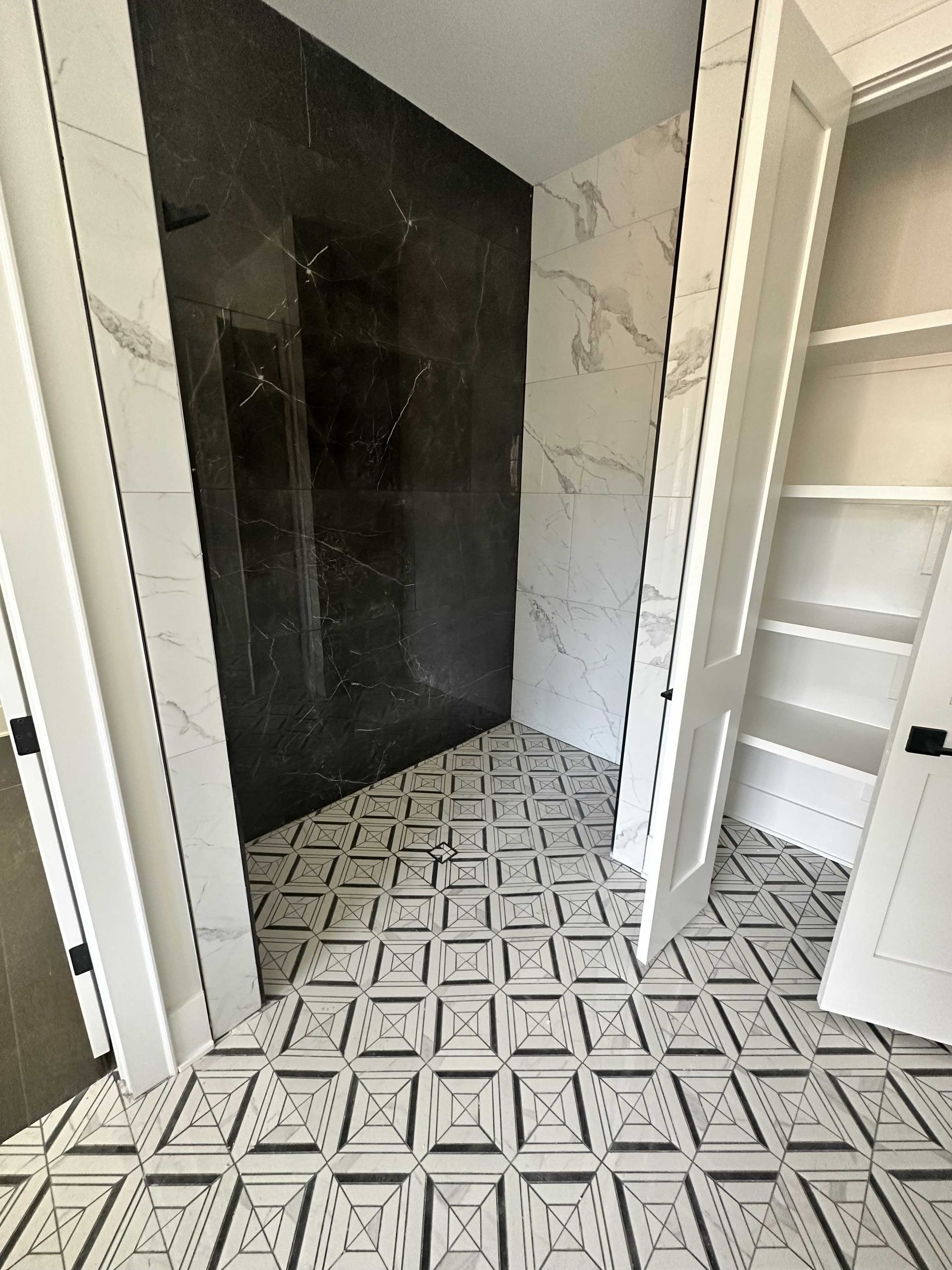 Bathroom with patterned tile floor, dark shower wall, and white shelving.