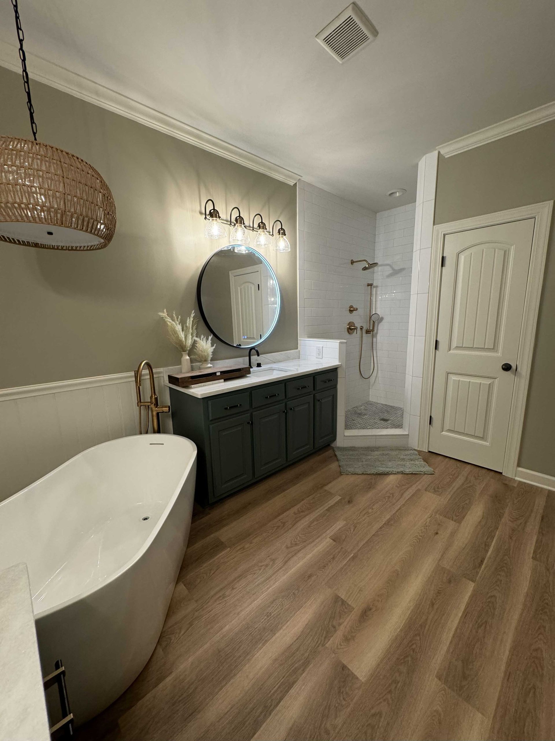 Modern bathroom with white tub, green vanity, and wood-look flooring.
