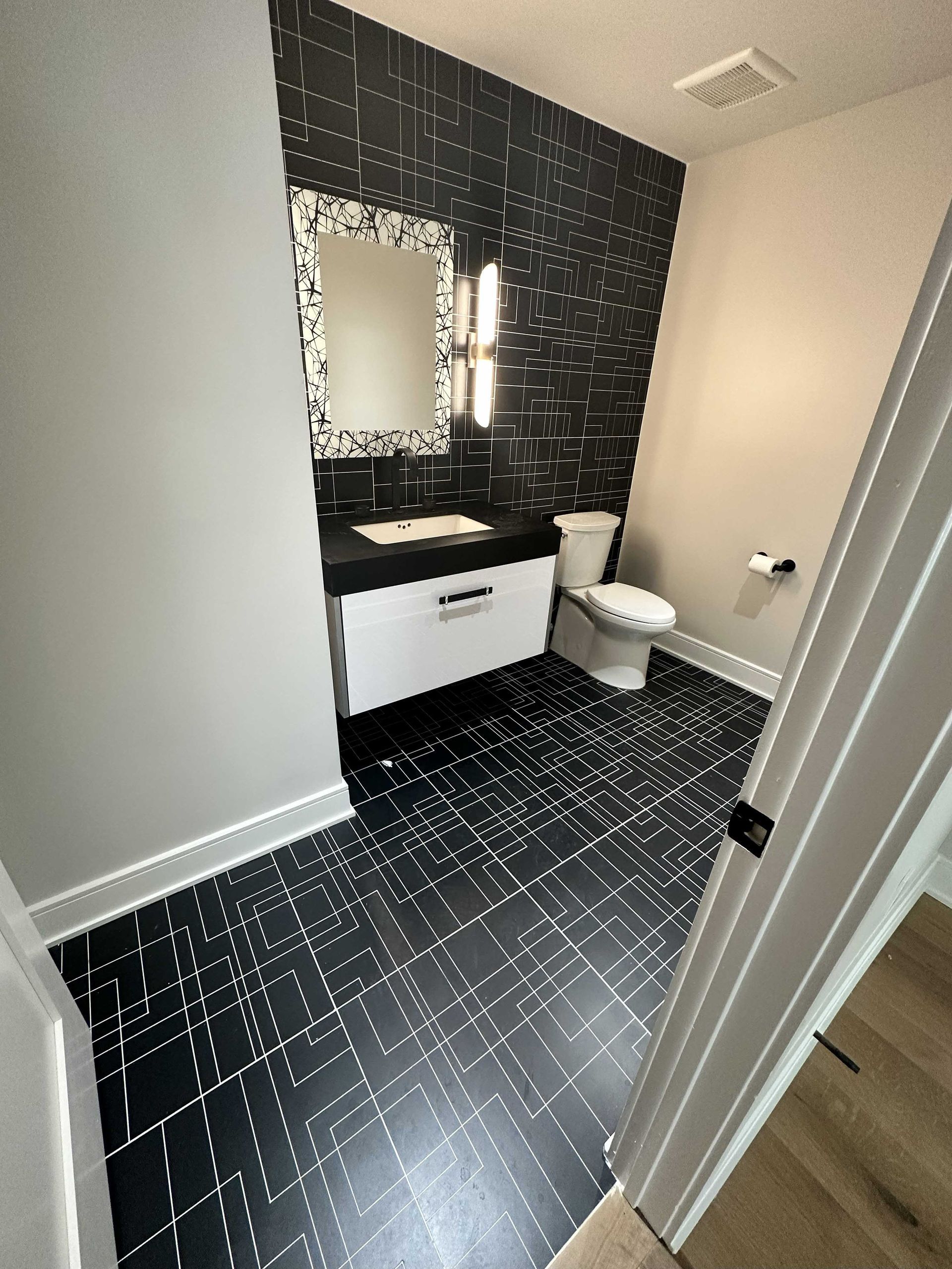 Black and white modern bathroom with tiled walls and floors, white vanity, and toilet.