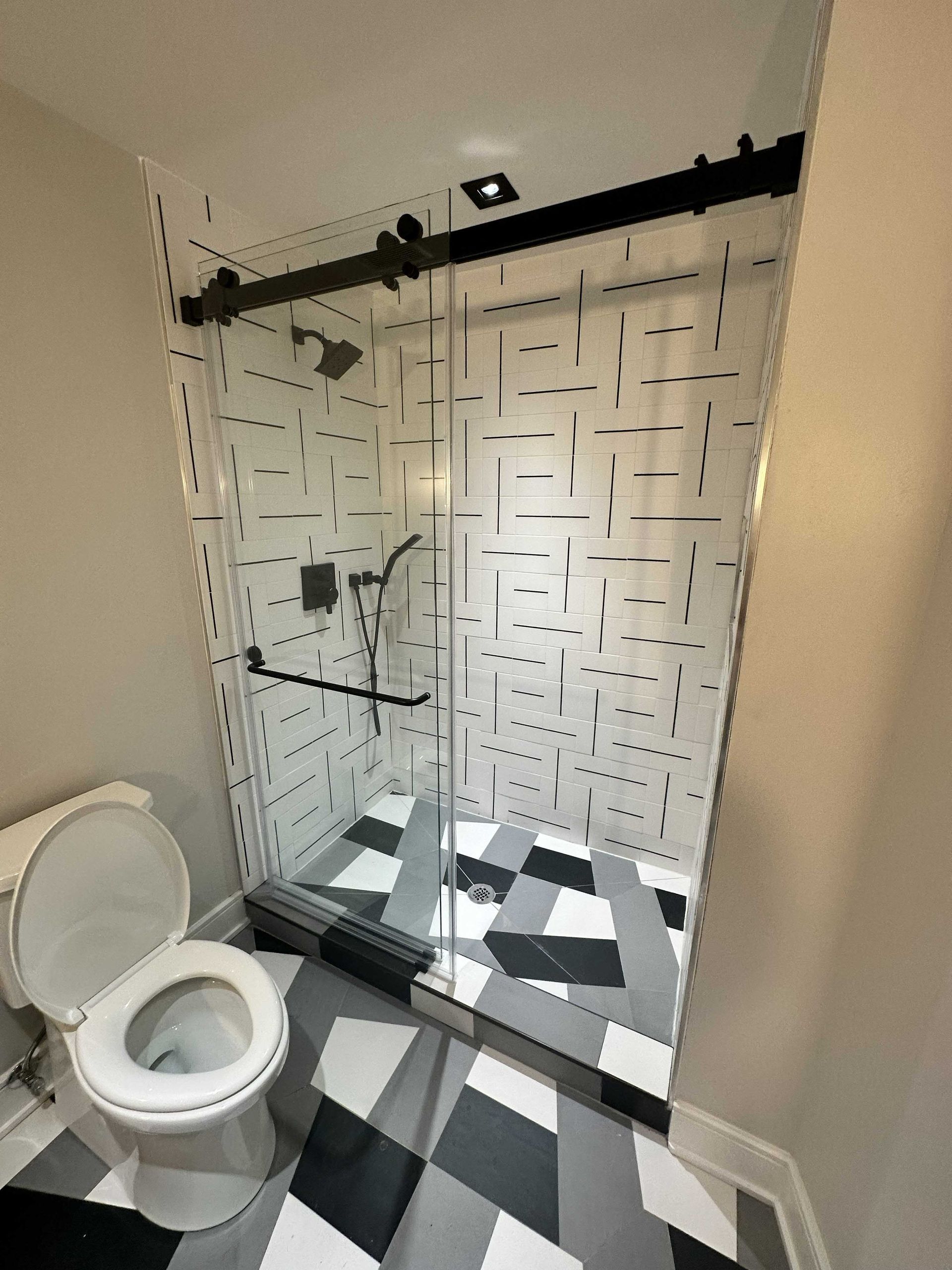 Bathroom with glass shower, patterned tile floor, and a toilet.
