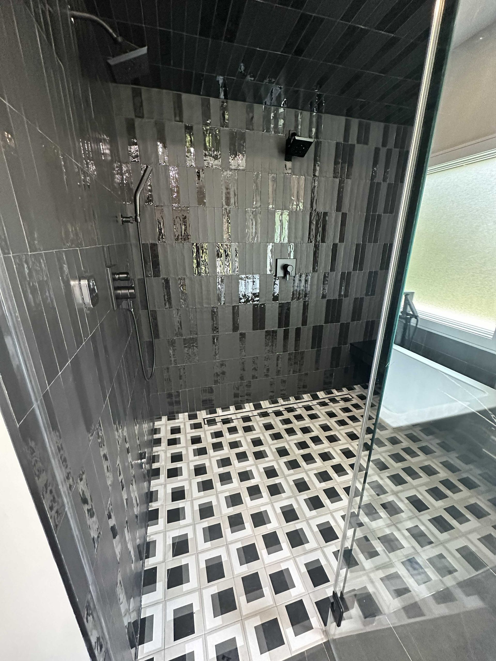 Black tiled shower with a patterned floor, glass door, and silver fixtures.