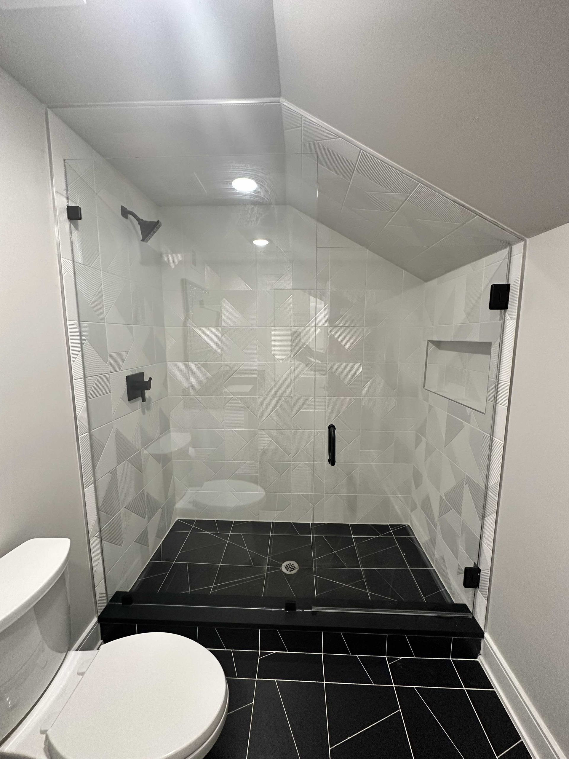 Modern bathroom with glass shower enclosure, black and white tile, and white toilet.