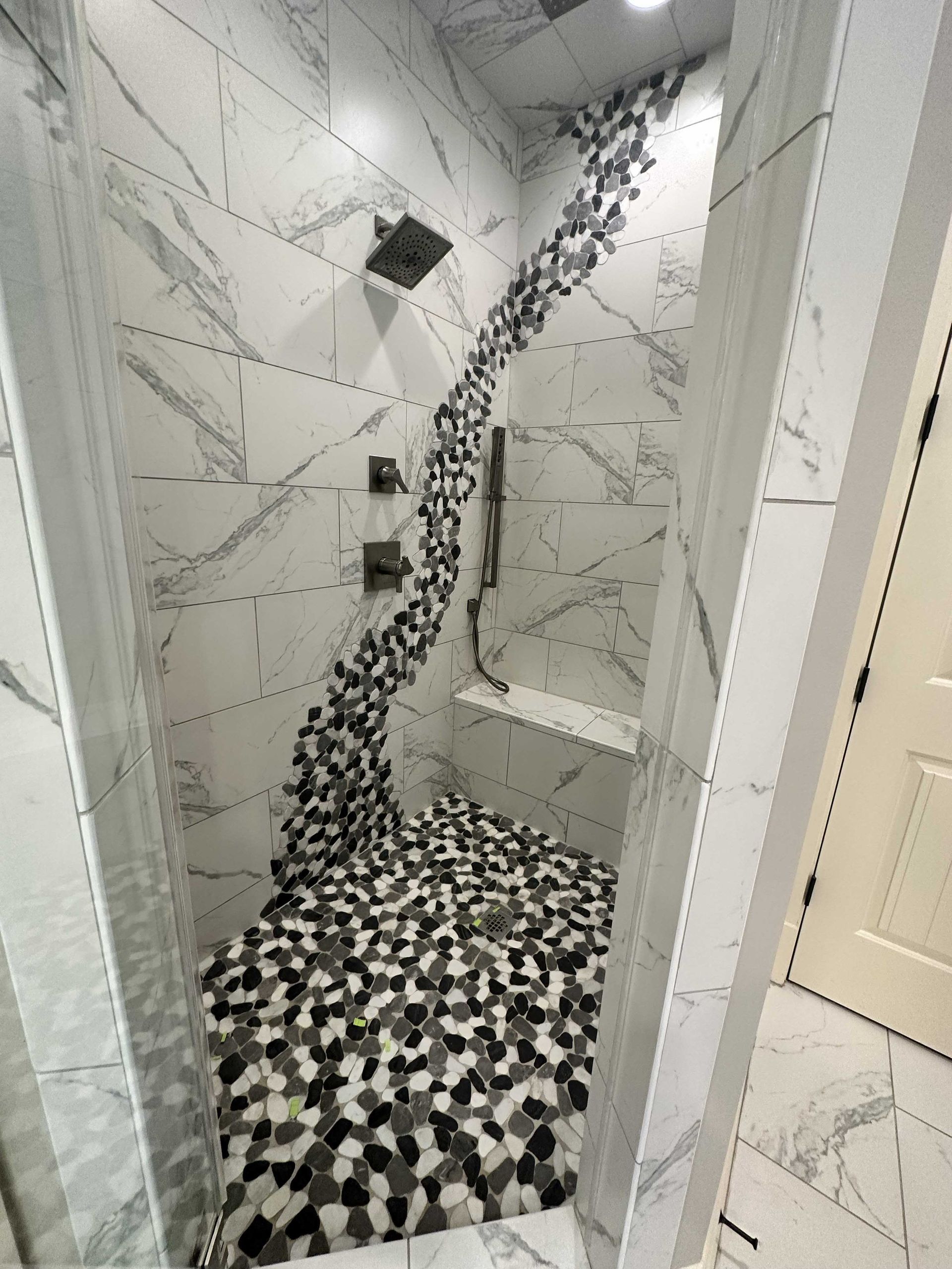 Shower with white marble walls, dark pebble floor, and a wave of black, white, and gray stones.