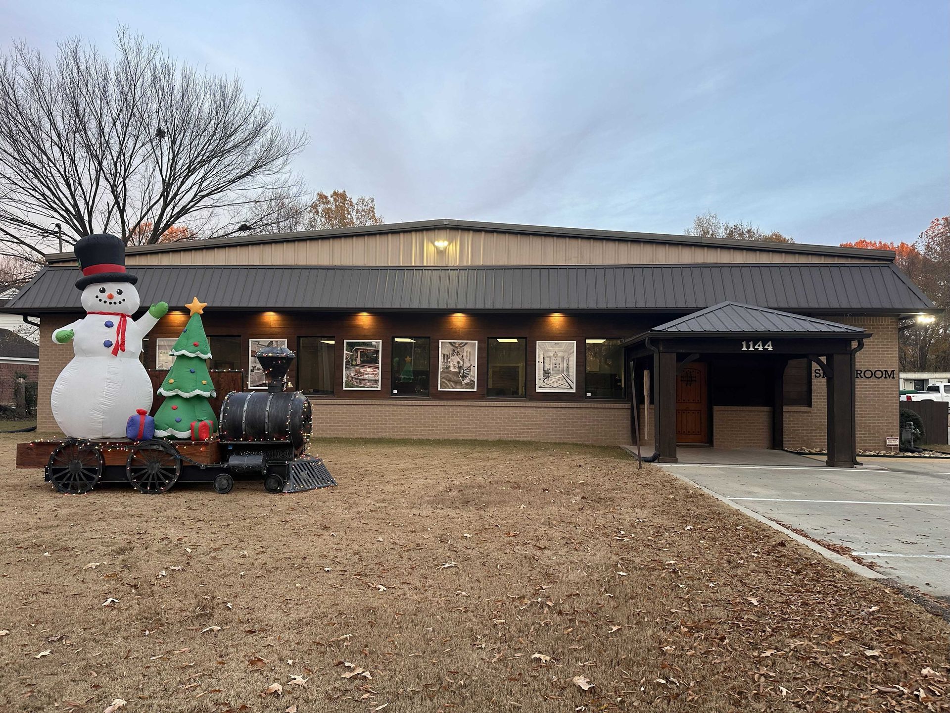 Building with Christmas decorations: snowman, tree, train. Brown brick, green grass, and cloudy sky.