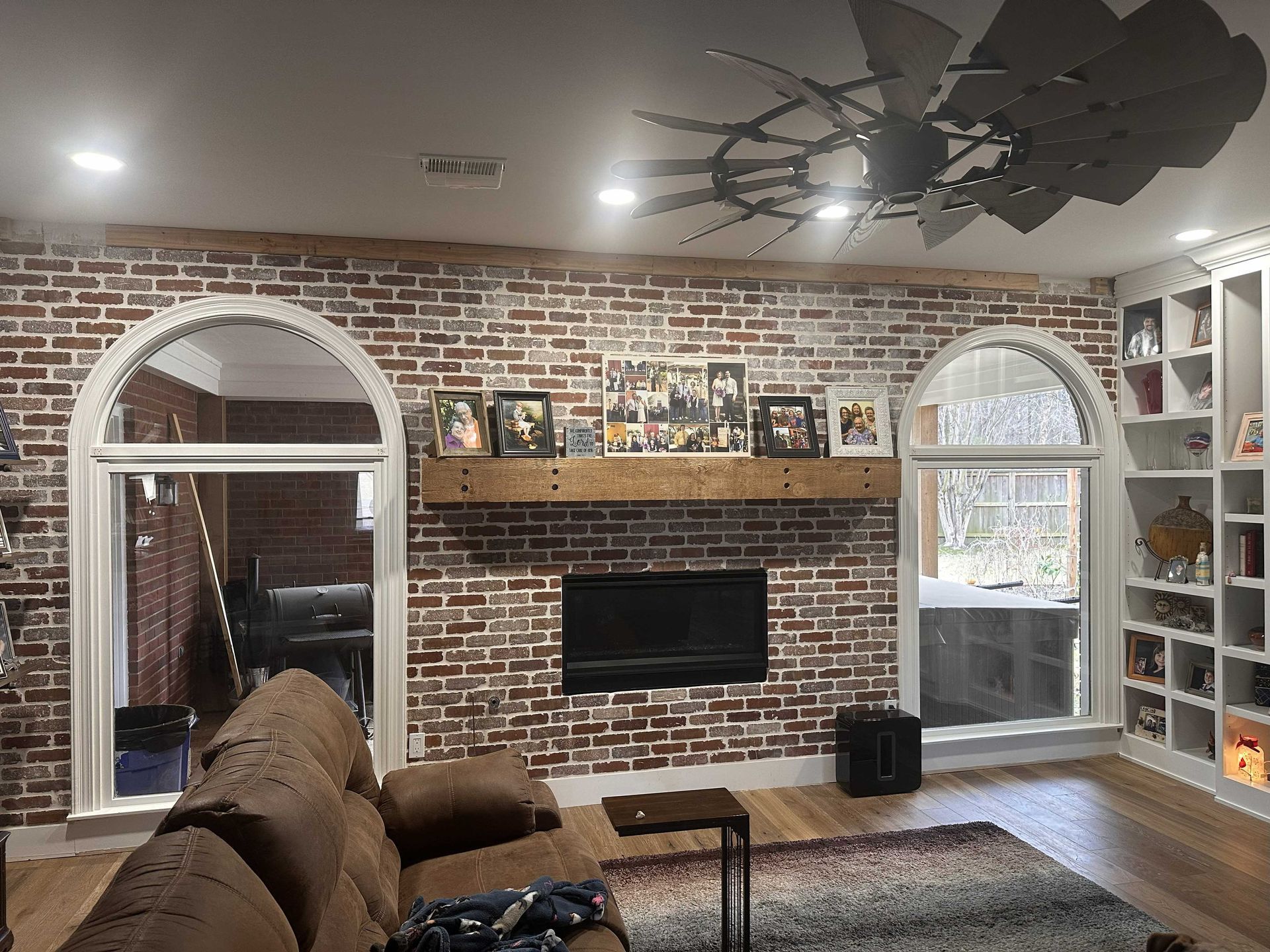 Living room with brick wall, arched windows, fireplace, and built-in shelves.