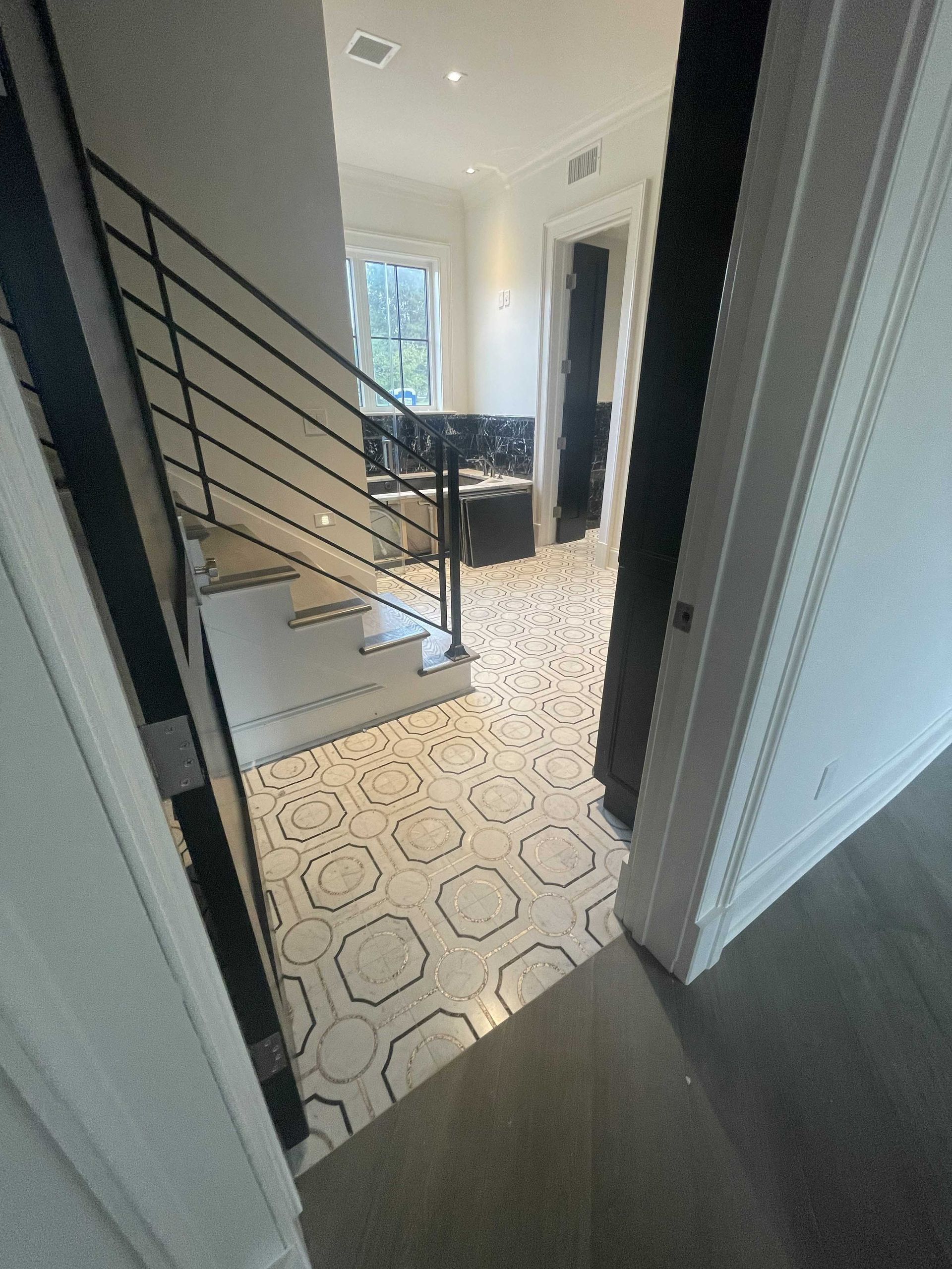 Staircase with black railing and geometric tiled floor, viewed from a doorway.