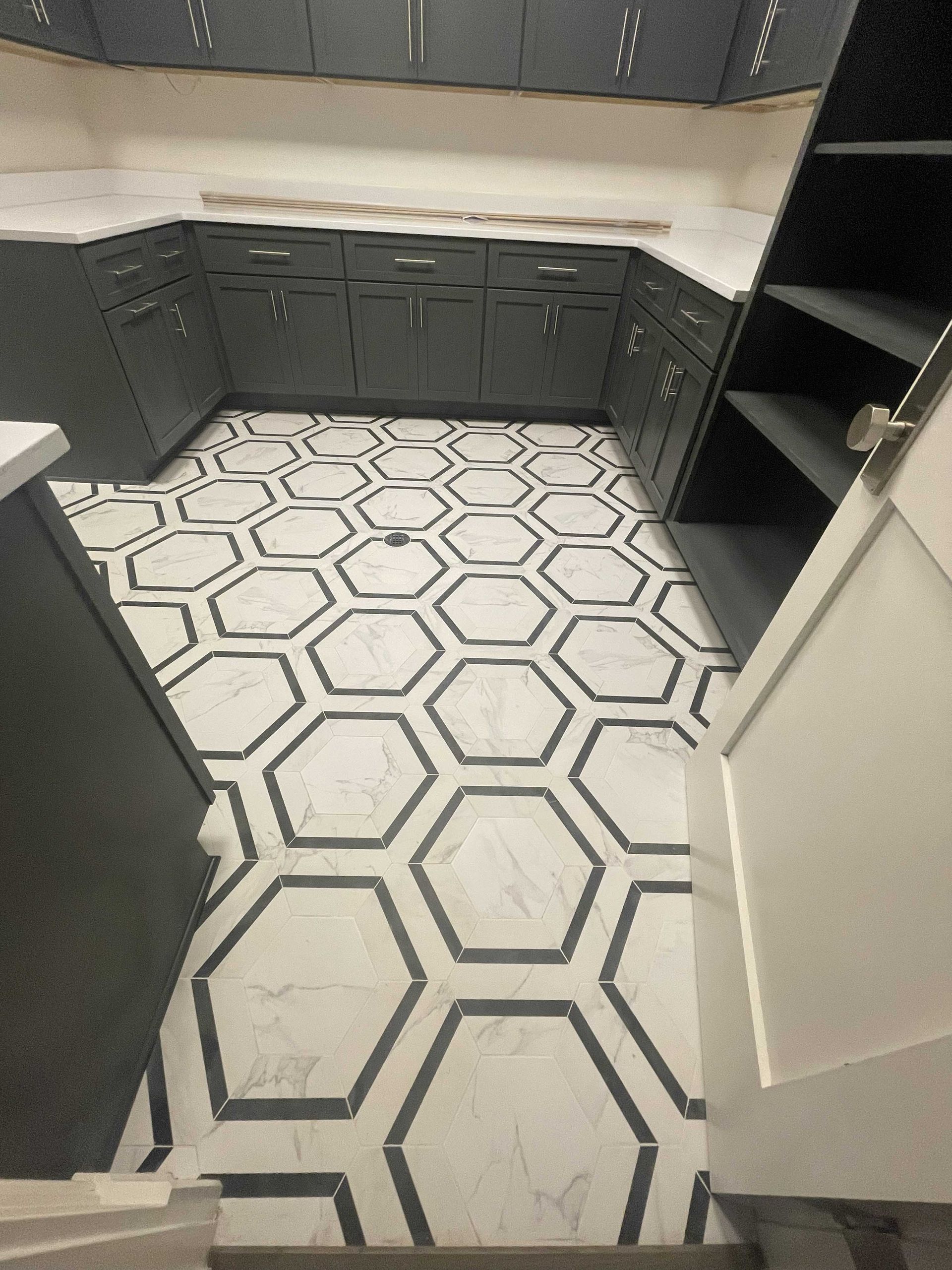Hexagon-tiled kitchen floor with dark gray cabinets. White countertop. Built-in pantry on the right.