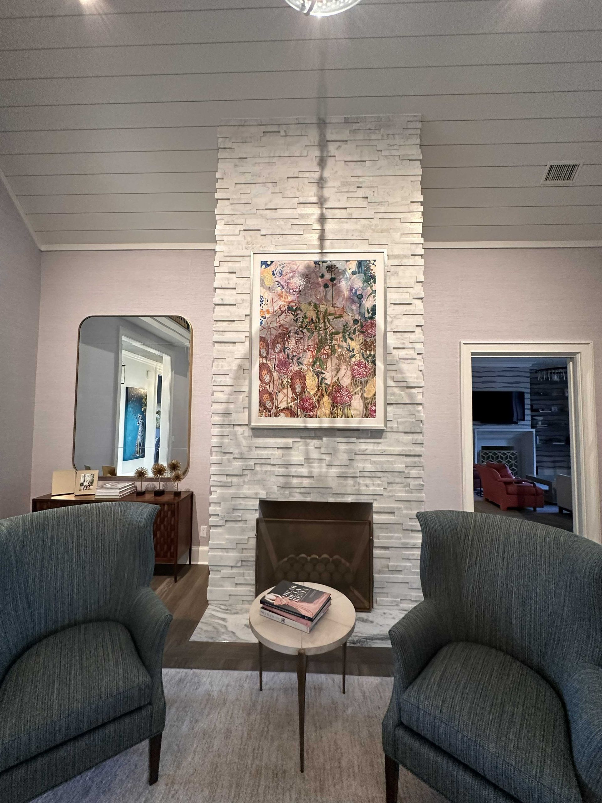Living room with fireplace, chairs, and artwork; stone facade, gray and blue color scheme.
