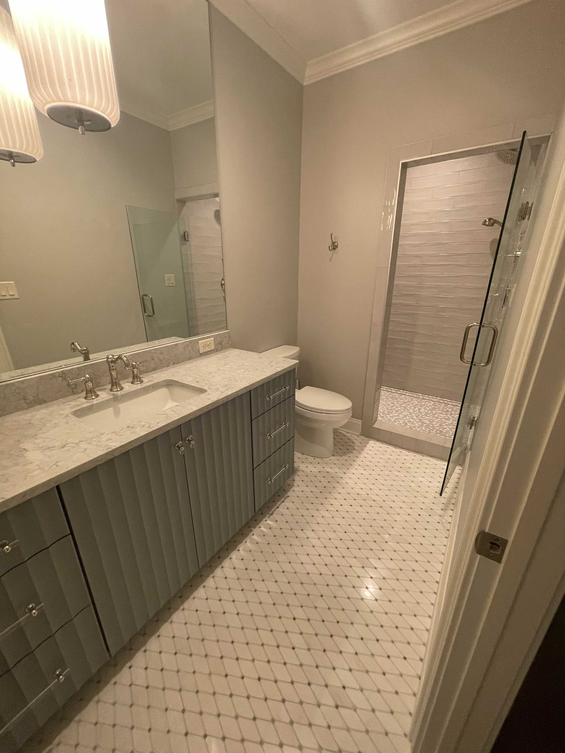 Bathroom with light blue vanity, white countertops, tiled floor, glass shower, and white toilet.