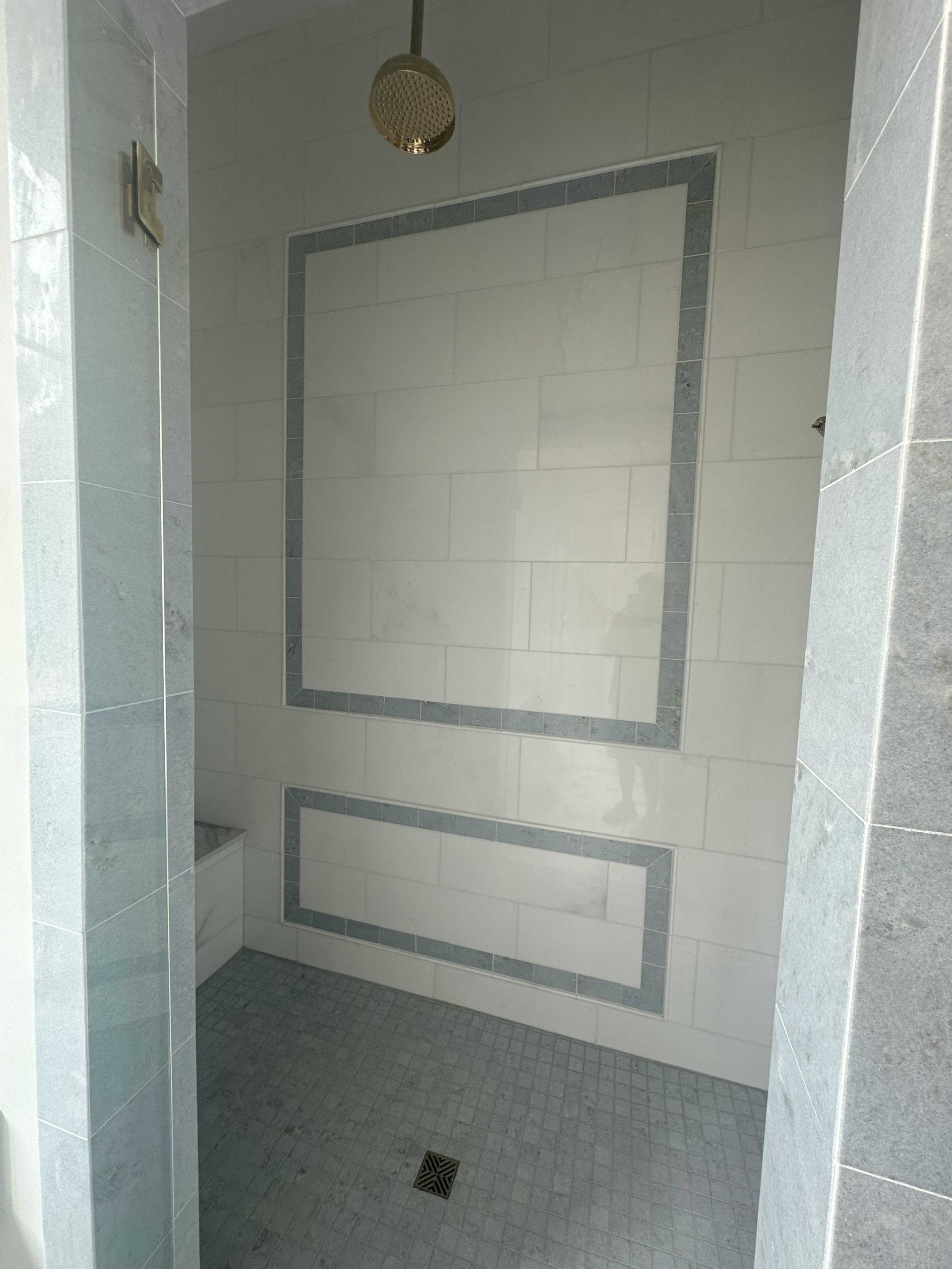 Bathroom shower stall with white and grey tile, and a gold showerhead.