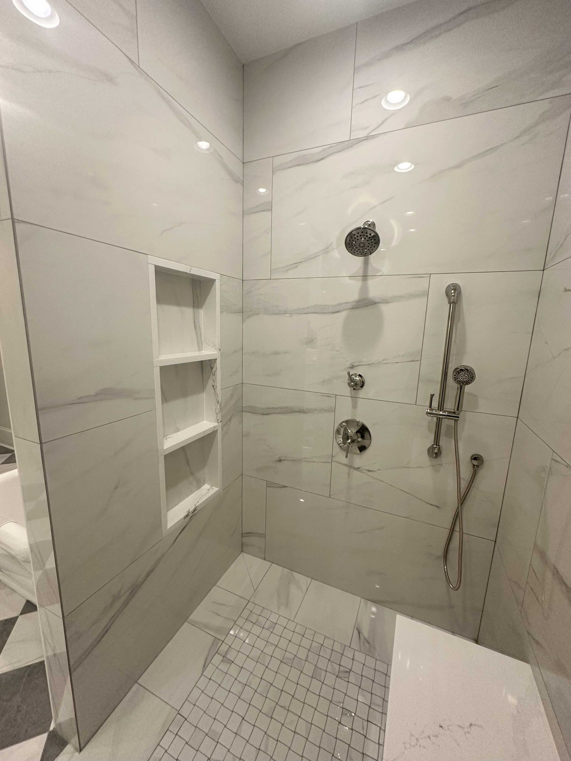 White tiled shower with built-in shelves, chrome fixtures, and a glass door.