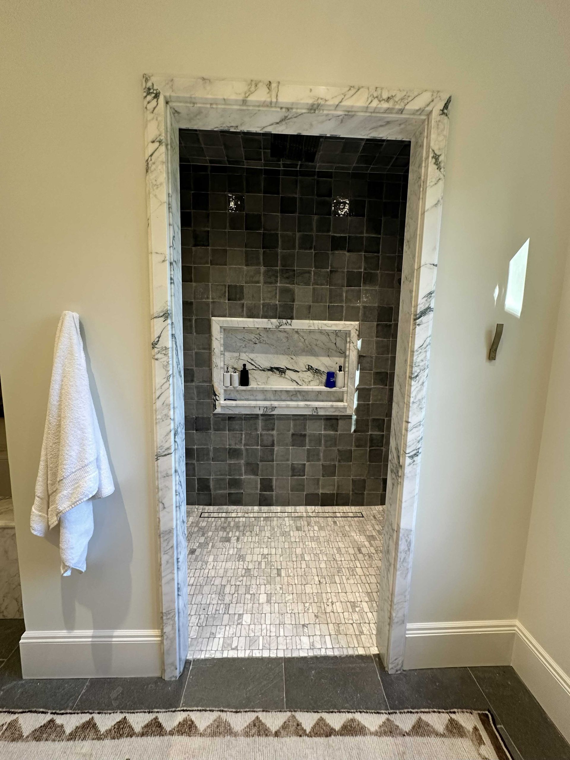 Bathroom doorway leading to a shower with gray tiles, marble trim, and a white towel on the left.