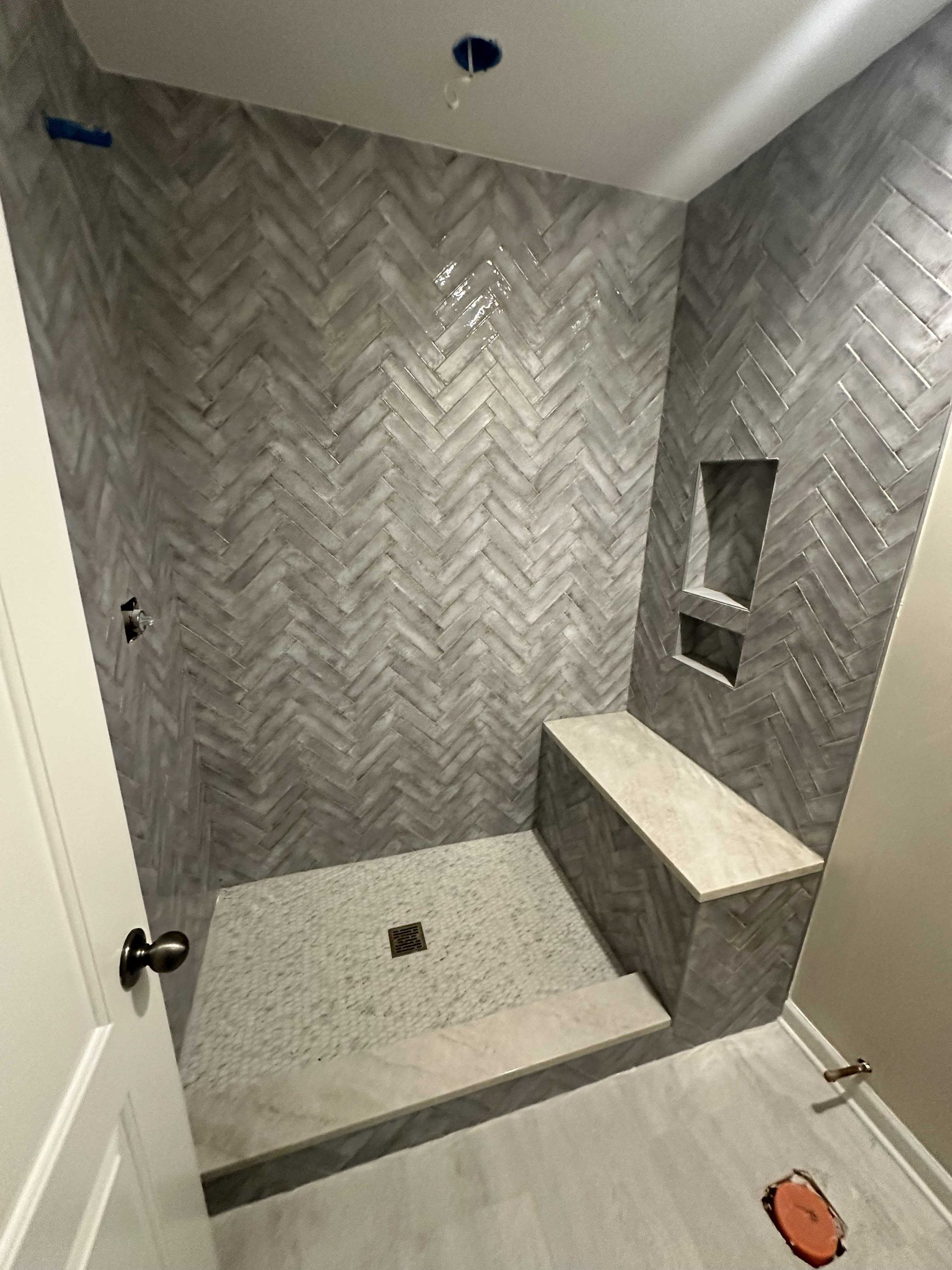 Shower with gray herringbone tiled walls, built-in bench, and terrazzo floor; wood-look tile.