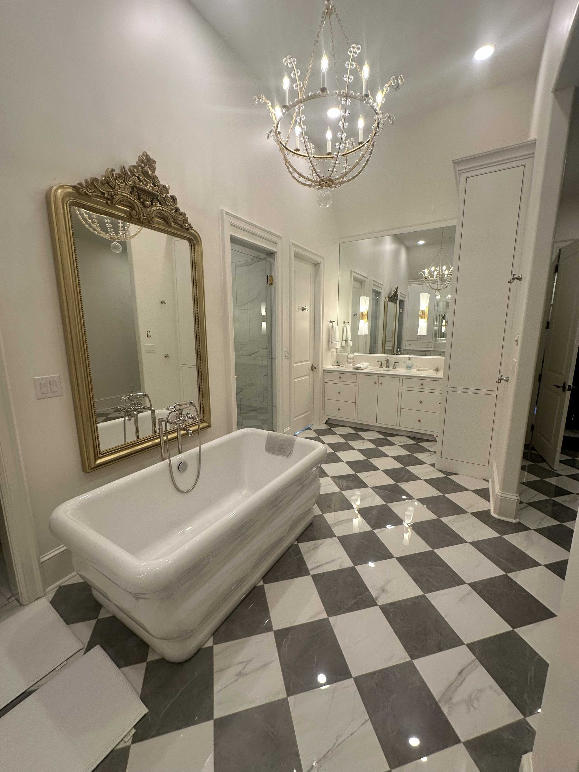 Luxurious bathroom with clawfoot tub, gold-framed mirror, checkerboard floor, and chandelier.