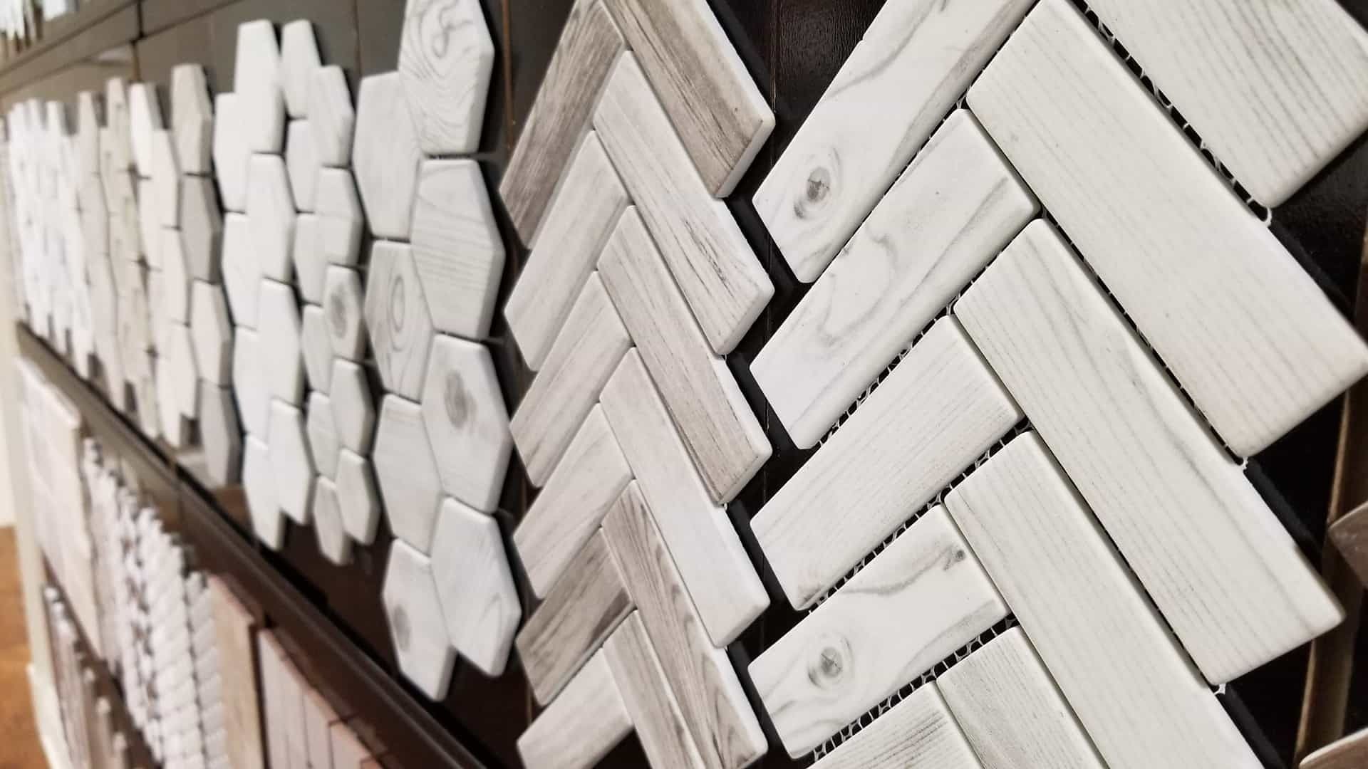 Display of various white and gray patterned tiles, including herringbone and hexagonal shapes.