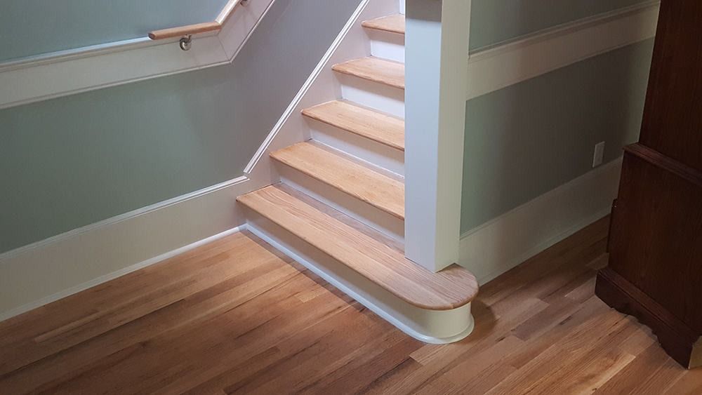 Staircase with light wood steps and handrail against a blue wall. White trim and hardwood floors.