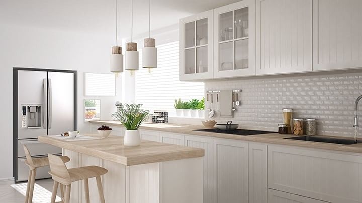 Bright white kitchen with a wooden island, stainless steel fridge, and hanging lights.