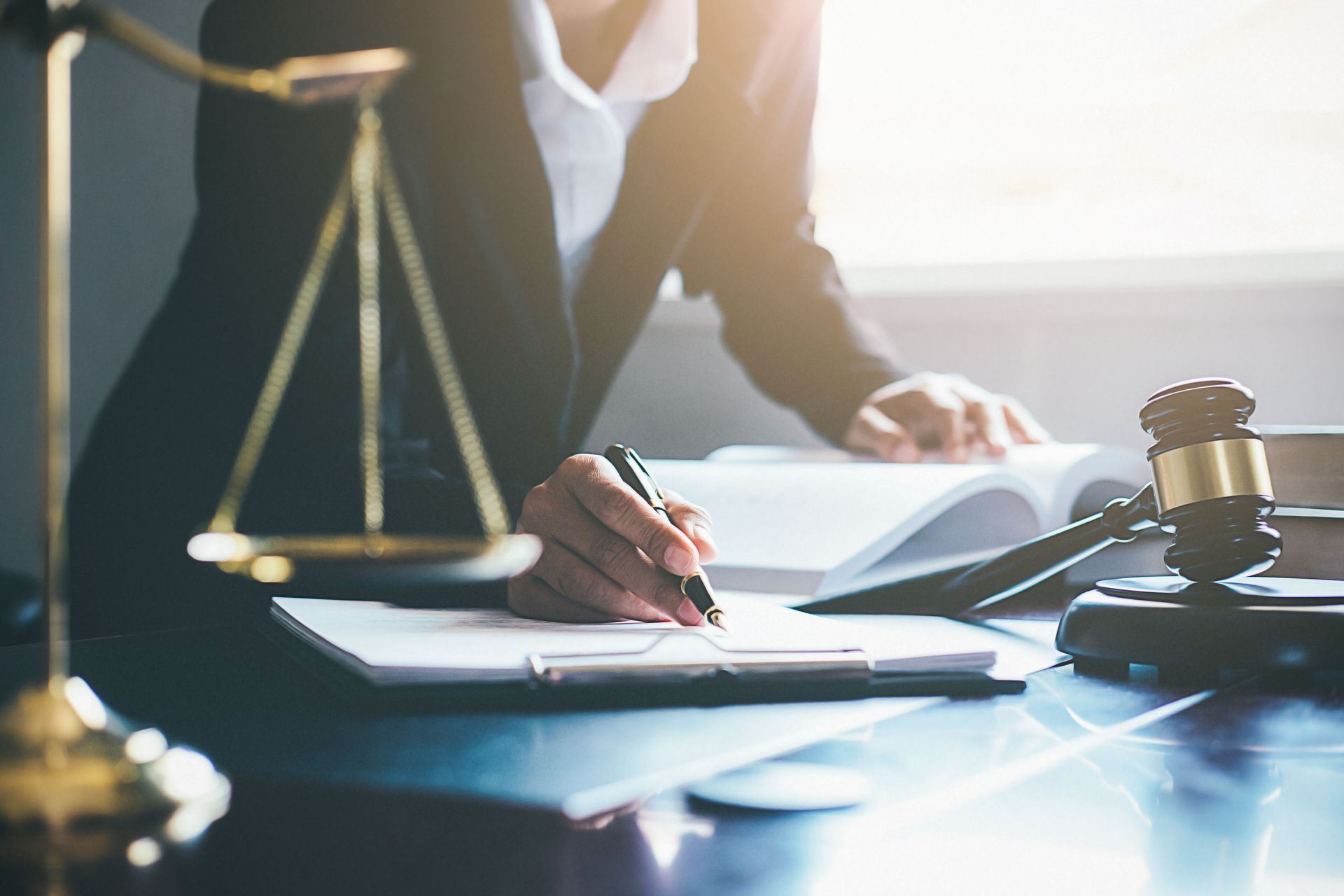 A person writing on a document at a desk with a gavel and scales of justice.