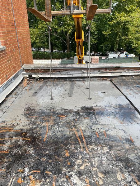 Forklift lifting supports on a deteriorated rooftop; brick building, trees in background.