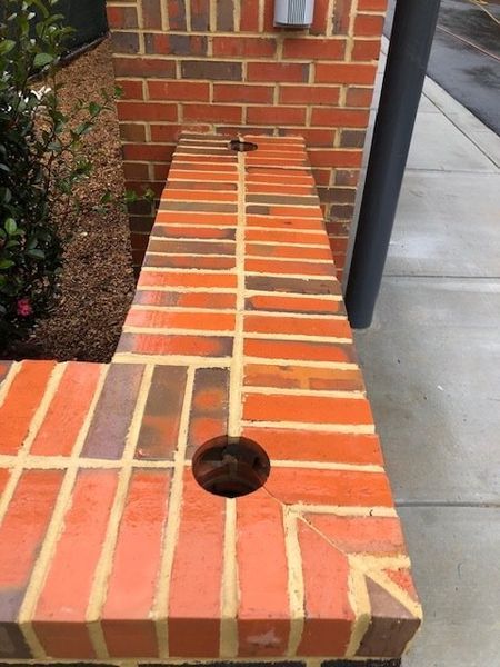 Brick bench with two holes, next to a brick wall and a black pole.