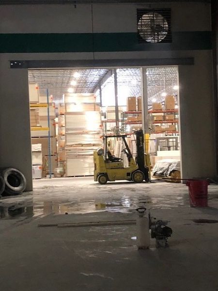 A yellow forklift sits inside a warehouse doorway. Shelves and boxes are visible in the background.