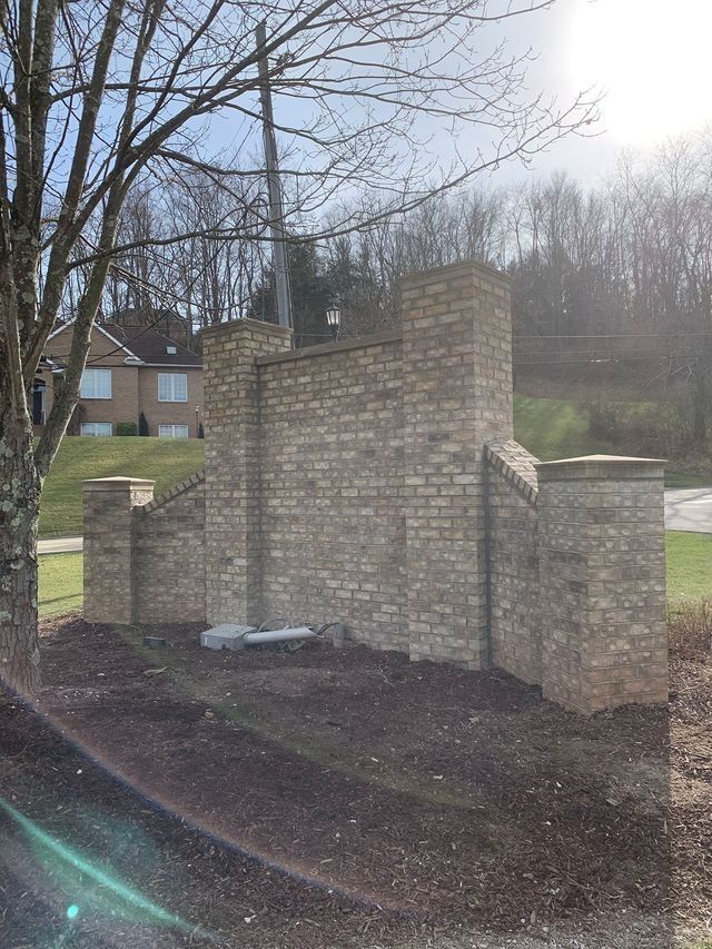 Brick wall entrance with pillars. Houses in the background. Overcast day.