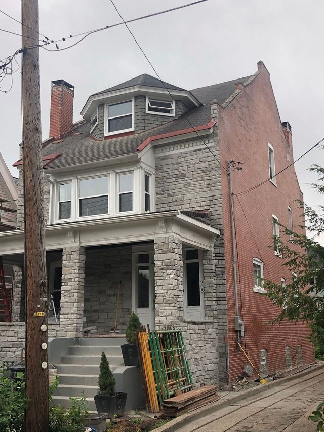 Two-story house with stone facade and red brick side, gray sky, steps lead to porch, utility pole in foreground.