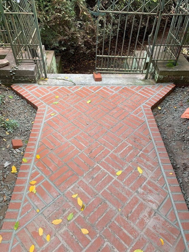 Brick pathway with intricate pattern, leading to metal gate in outdoor setting.