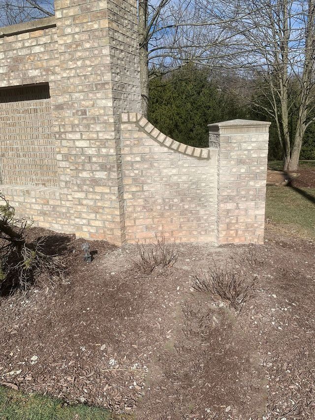 Brick wall section with curved top, topped with a column. Brown landscaping in front.