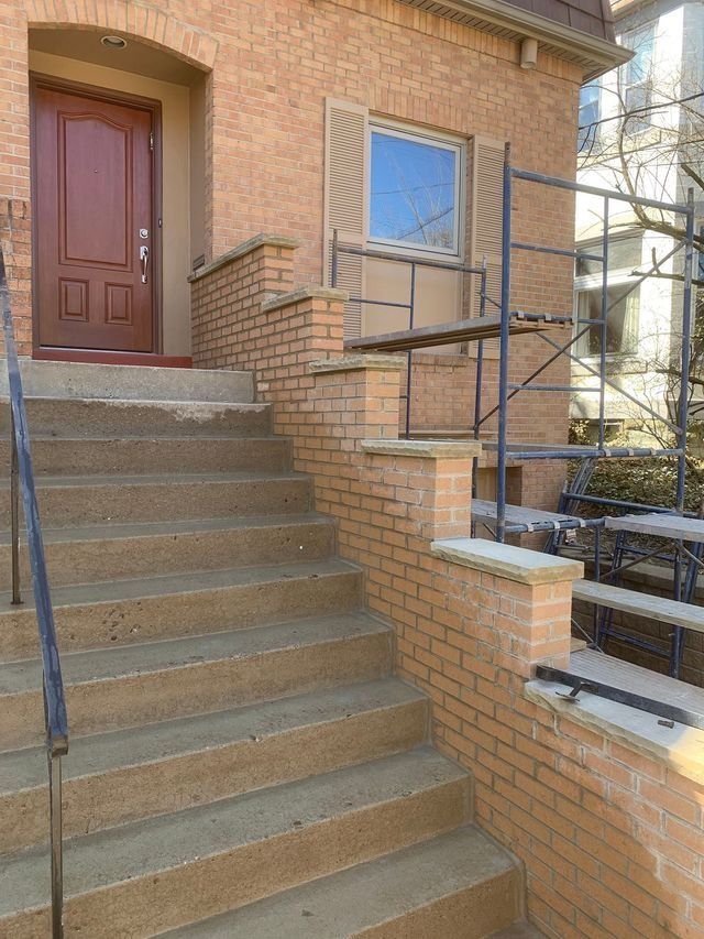 Brick building entrance with concrete steps and a red door. Scaffolding present.