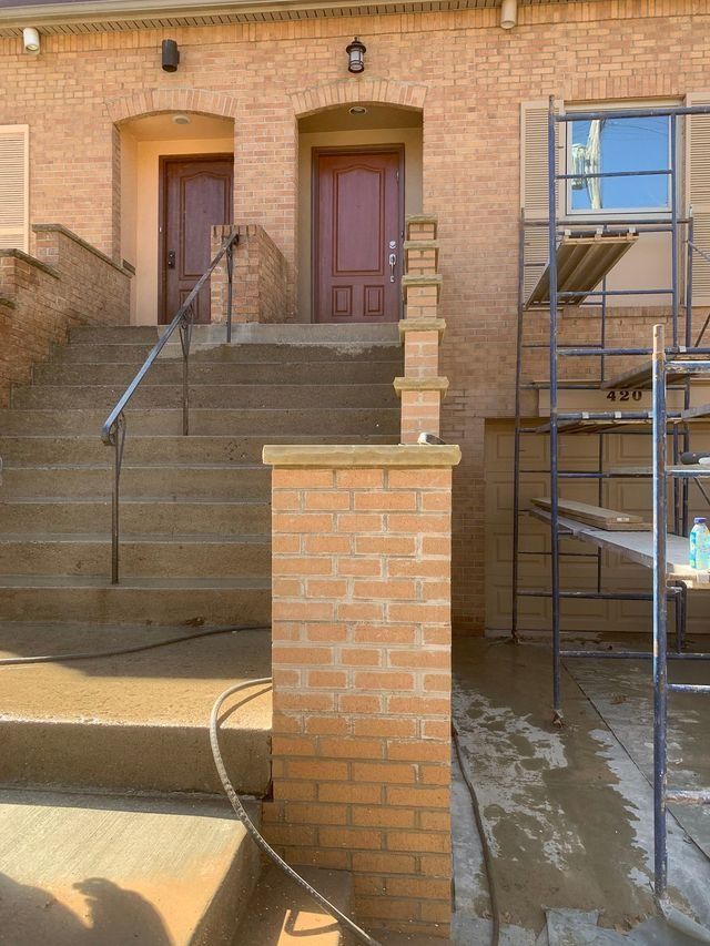 Brick building entrance with stairs, doors, and scaffolding. Brown bricks and doors, concrete stairs, metal railings.