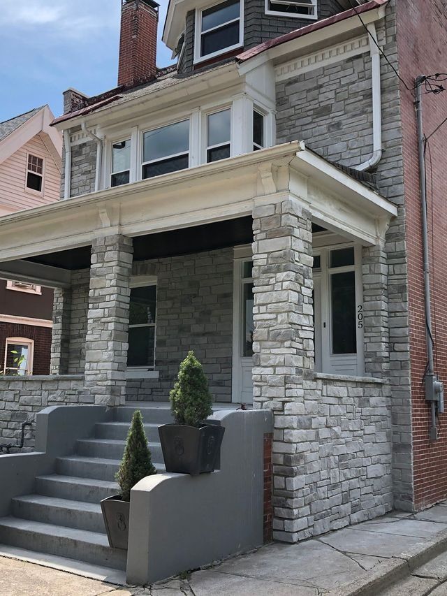 Stone-clad house with porch and stairs, topped with a decorative trim. Two potted plants stand on the steps.