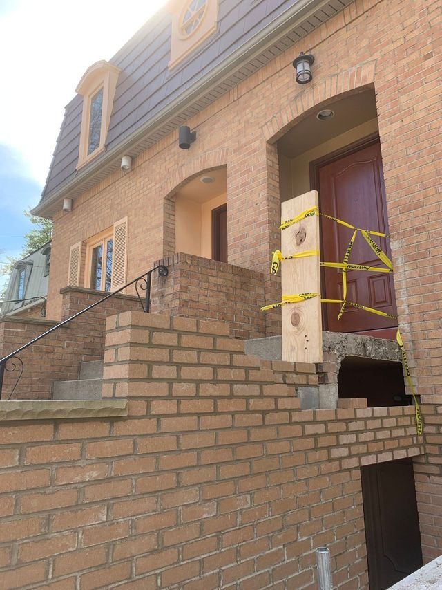 Brick building with damaged entrance; wooden board over door. Yellow caution tape.
