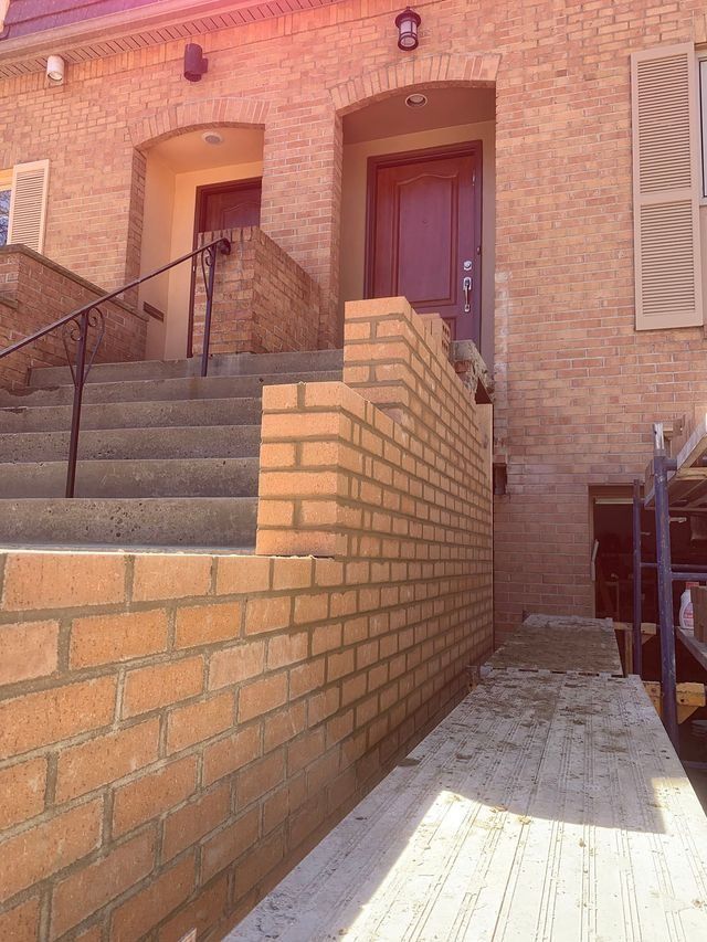 Brick wall being built near a set of stairs leading to a brick building's entrance.