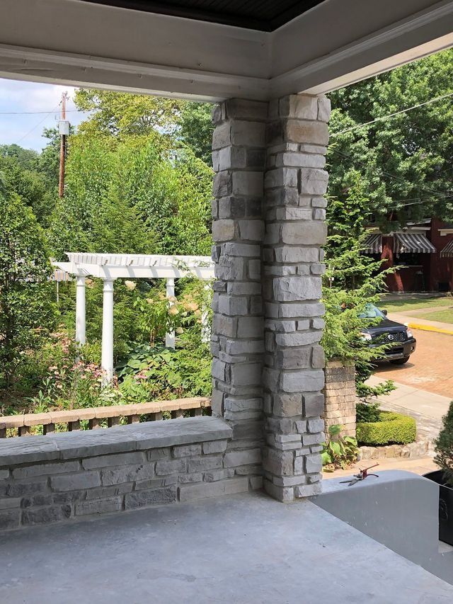 Stone porch column and wall with view of a garden and street.
