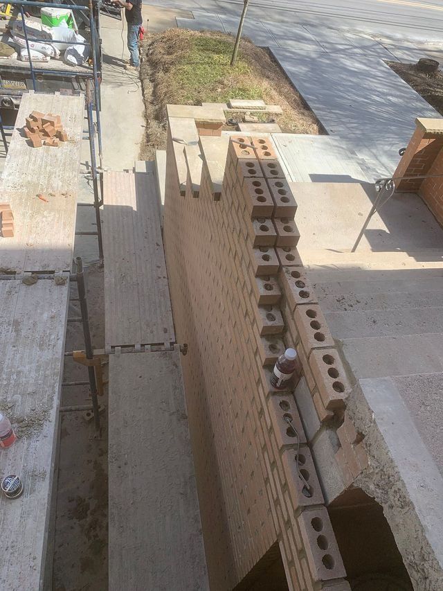 Brick wall construction, bricks stacked, worker on scaffolding, outdoors.