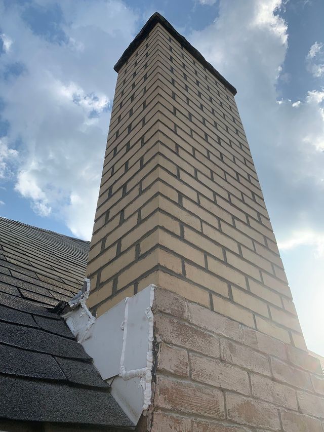 Brick chimney rising from a dark shingle roof, against a cloudy sky.