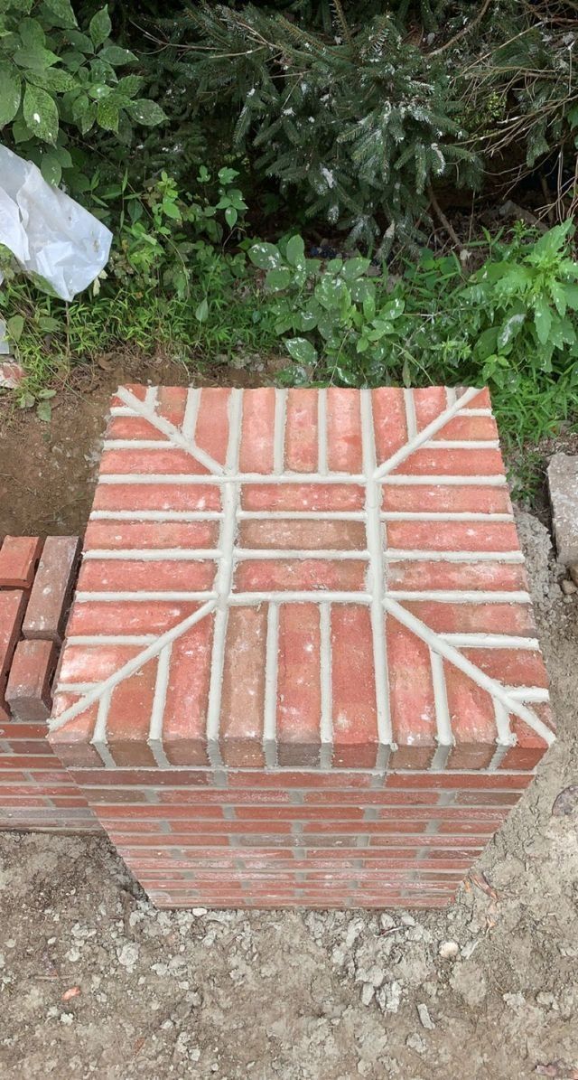 Brick pillar with patterned brick top. Red bricks, gray mortar, outdoor setting.