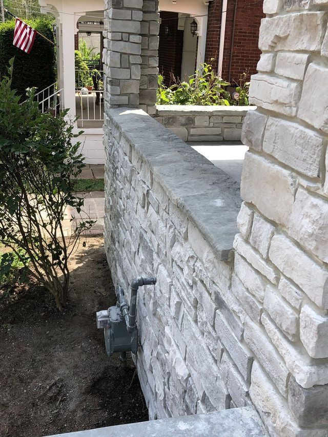 Stone wall and pillar of a house with a light-colored stone facade and a walkway.